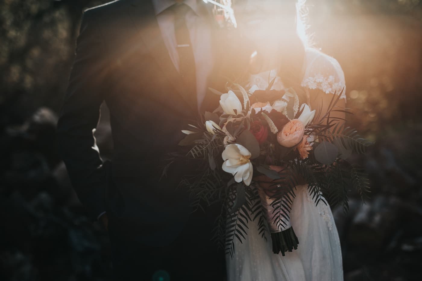 Bride and groom laughing beneath a wind-caught veil at golden hour